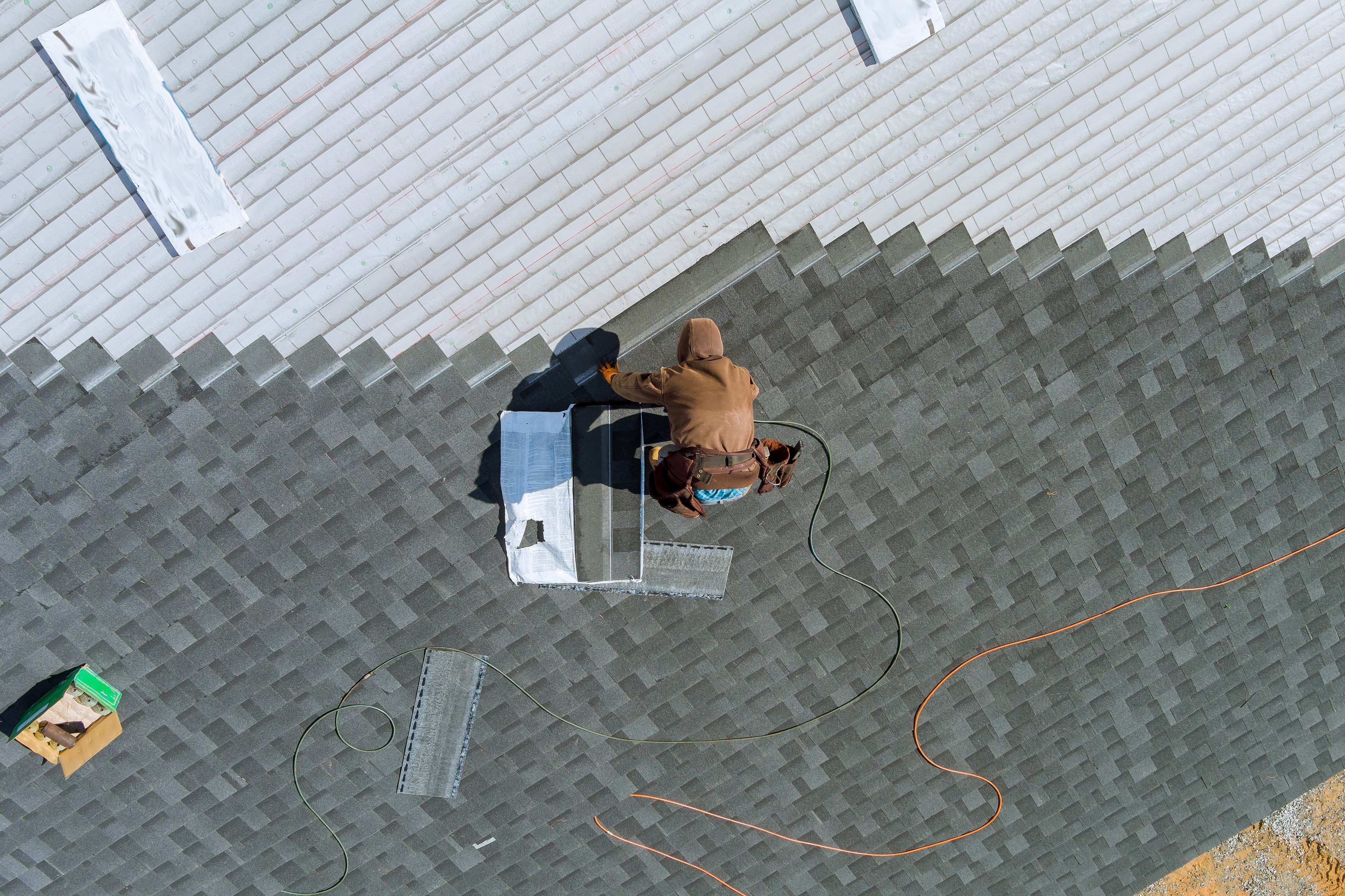Aerial view of a roofer using an air hammer to install asphalt shingles on a residential St. Louis home.